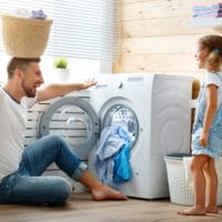 Happy family man father householder and child in laundry with washing machine