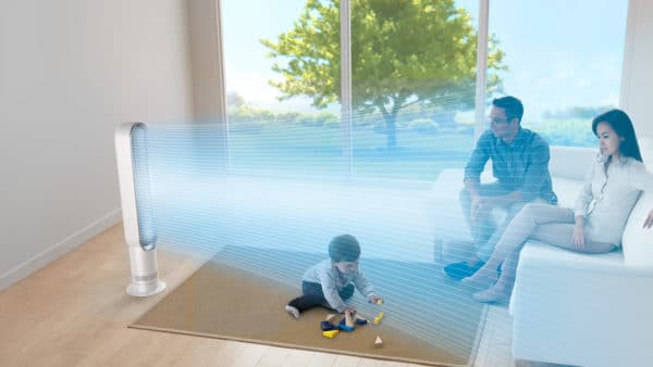 Dyson Turmventilator im Beispielbild im Einsatz. Zu sehen ist ein Raum mit Sofa und zwei erwachsenen Personen auf dem Sofa. Auf dem Boden spielt ein kleines Kind, während ganz links der Ventilator im Einsatz ist 