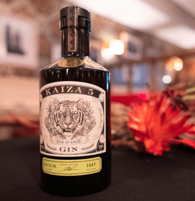 Flasche Kaiza 5 Gin steht auf einem schwarzen Tisch vor einer bunten Blume und in einem hellen beleuchteten Raum