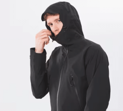 Ein Mann trägt die Quechua MH500 Regenjacke in schwarz mit hochgezogener Kapuze