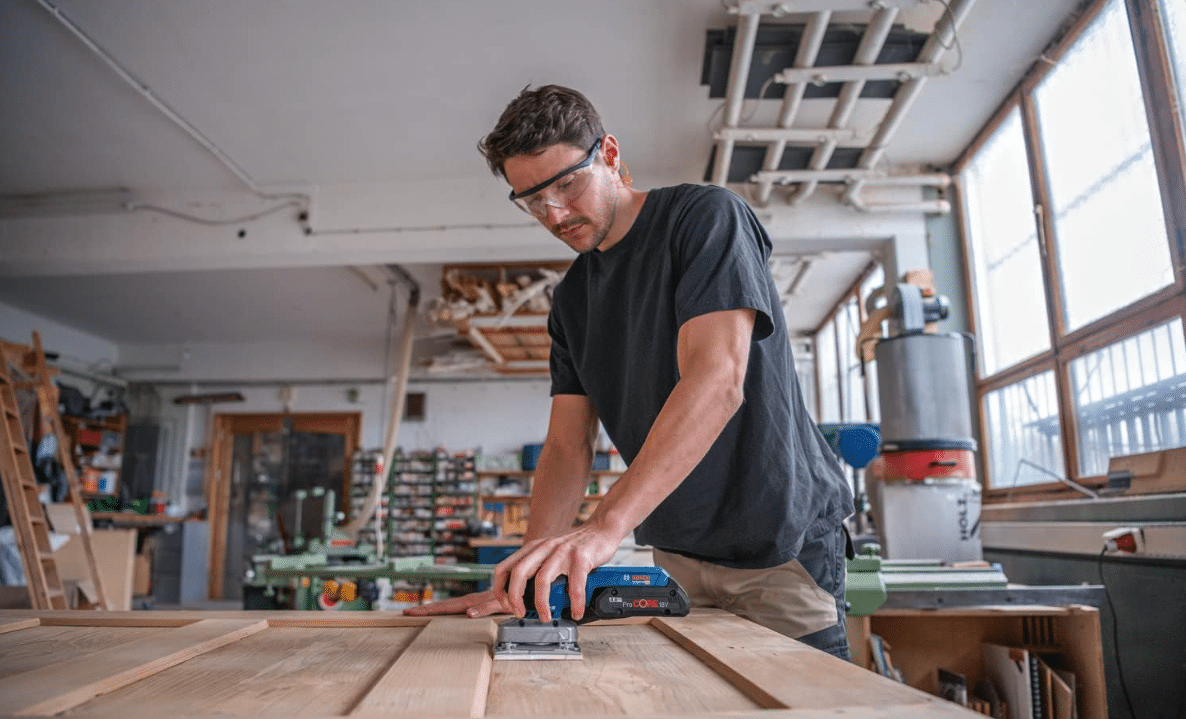 Ein Mann arbeitet mit dem Bosch Professional 18V System Akku Schwingschleifer an einer Tür in seiner Werkstatt